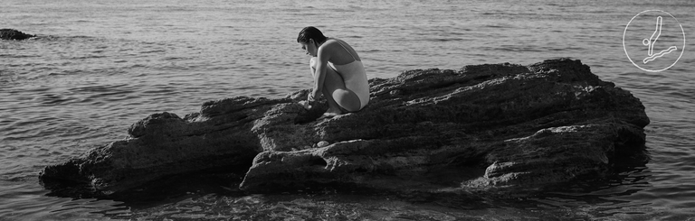 Person sitting on a rock in the water, black and white photo