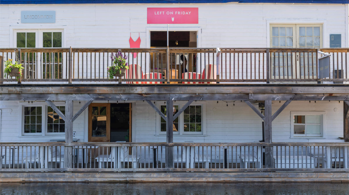 A white building with multiple decks and railings, featuring a red 'LEFT ON FRIDAY' sign above the entrance and outdoor seating on the upper balcony.