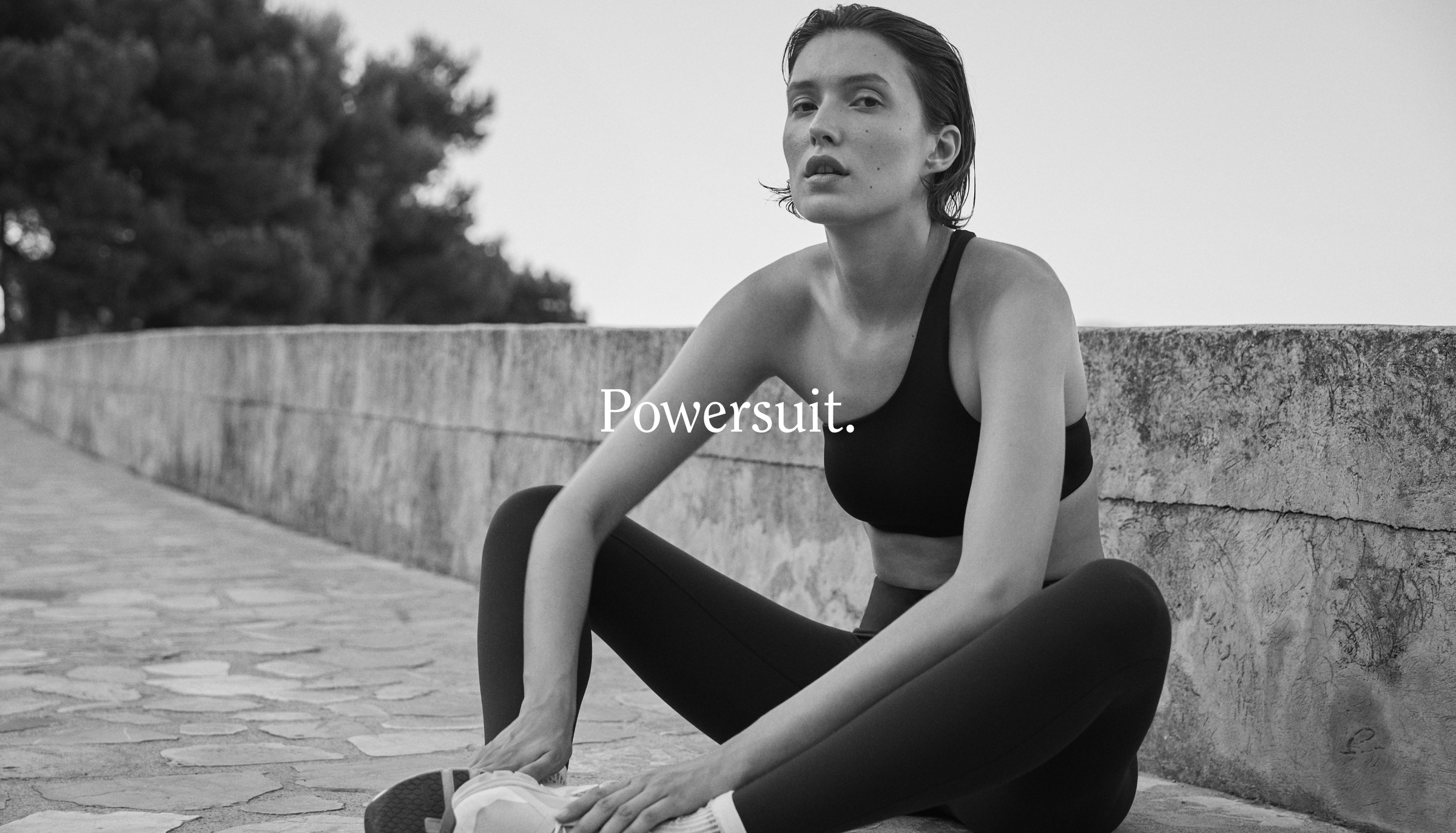 Woman in Left On Friday athletic wear sitting on a stone wall with 'Powersuit' text overlay.