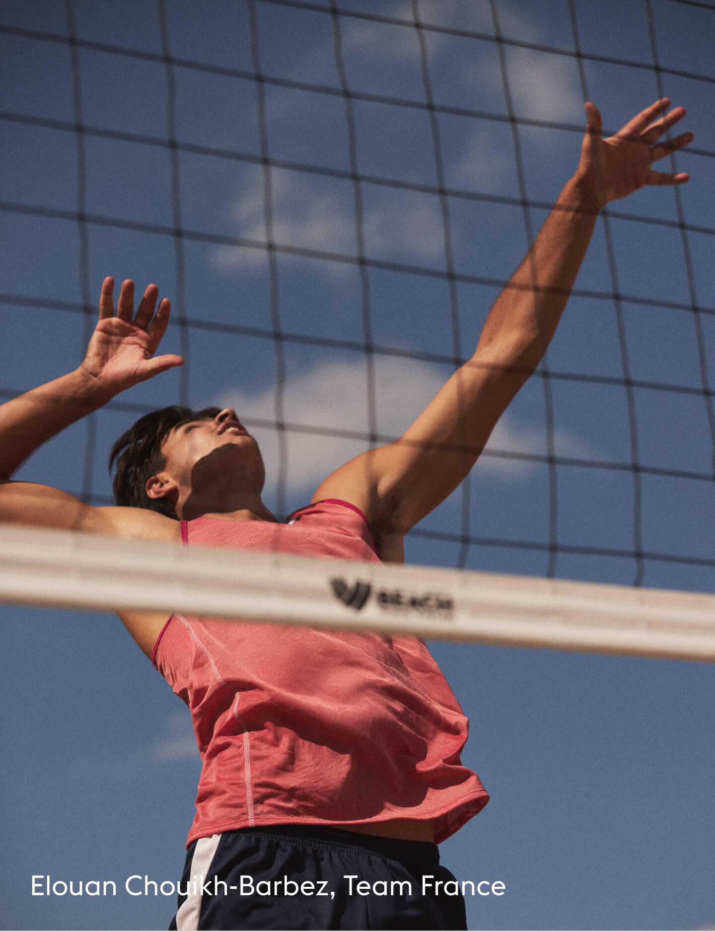 A male volleyball player in a pink sleeveless shirt and dark shorts jumps to spike the ball over a net against a blue sky background. Text at the bottom reads 'Elouan Choukhi-Barbez, Team France'.