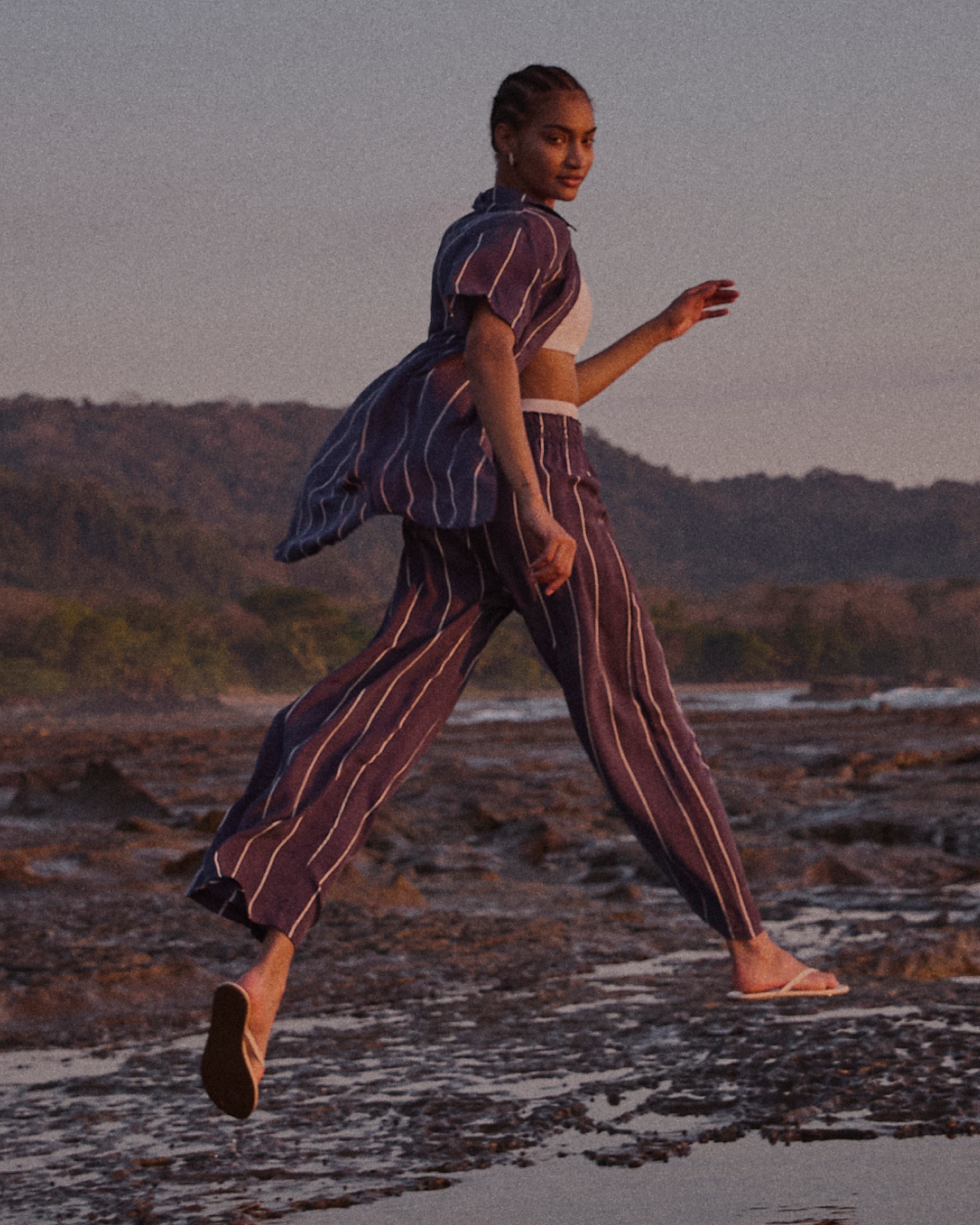 Woman in a striped Sport Silk set walking on a beach with a scenic background
