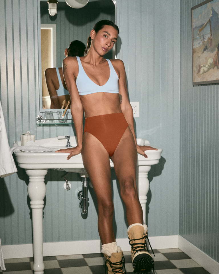 Person wearing a Blue Skies Plunge top and Bronze Hi Hi bottoms in a bathroom.