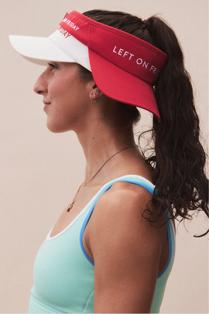A woman in profile wearing two athletic visors: a red visor with white text reading 'LEFT ON F.