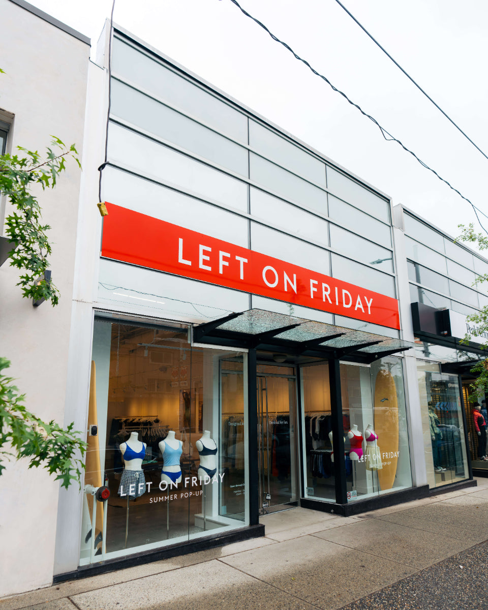 A storefront for a clothing store with a large red sign reading 'LEFT ON FRIDAY' above glass windows and doors. Mannequins and garments are visible inside, and the building facade is light gray with black window frames.