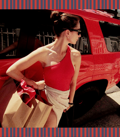 Woman in a red Shoreline Suit and beige sarong next to a red car on a sunny day.