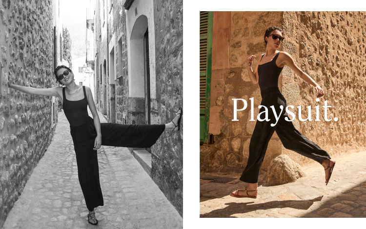 Woman in black Streamline Suit and Sheer Stripe Day Trip Pant posing on a stone street with 'Playsuit' text overlay.