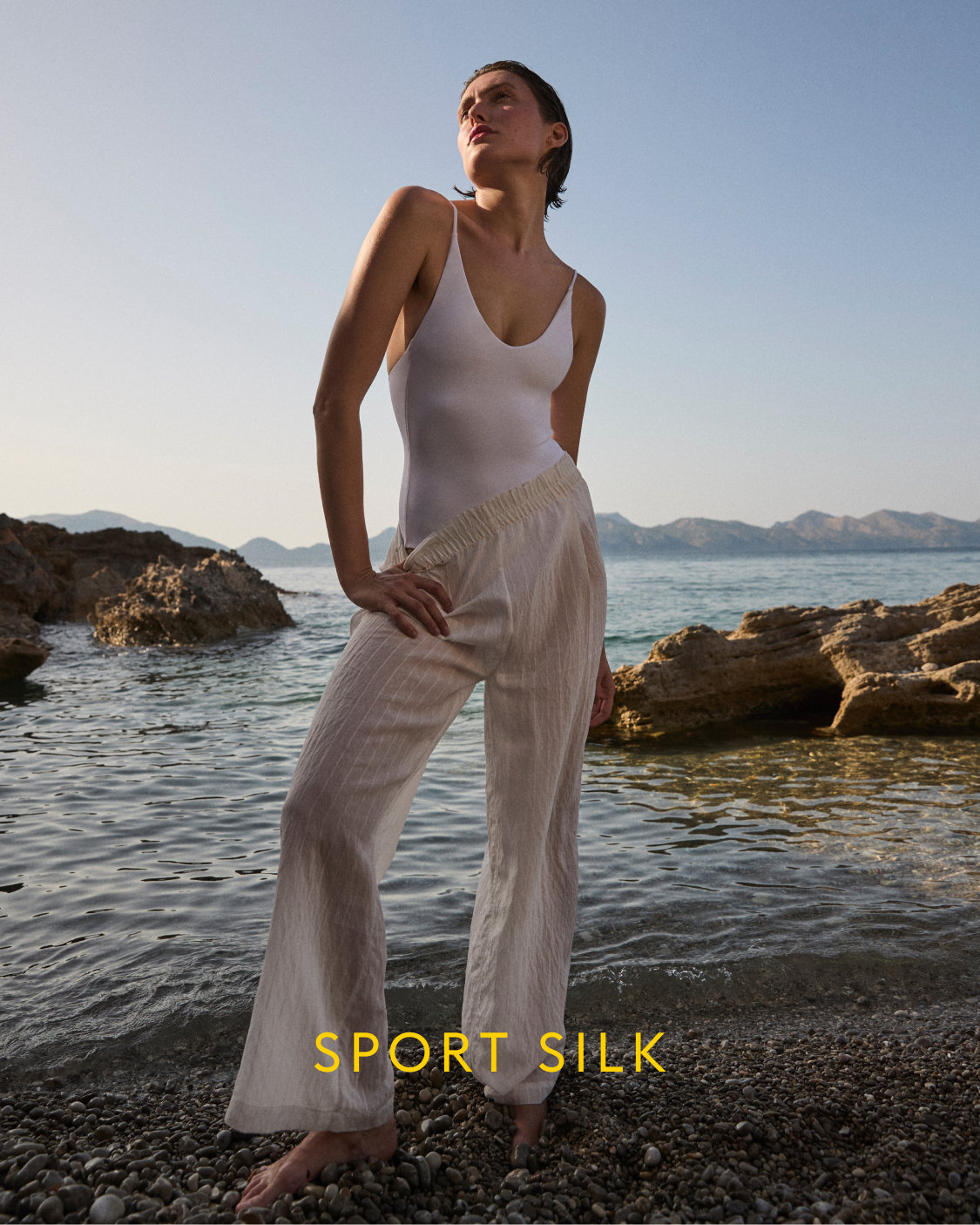 Person wearing a white Sunday Suit and Day Trip Pant by a body of water with 'Sport Silk' branding.