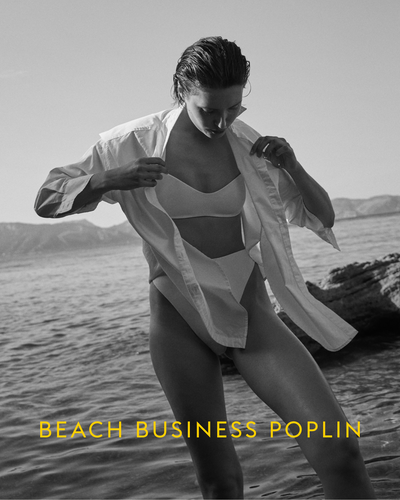 Person in a swimsuit with a white poplin shirt on a beach, with 'Beach Business Poplin' text.