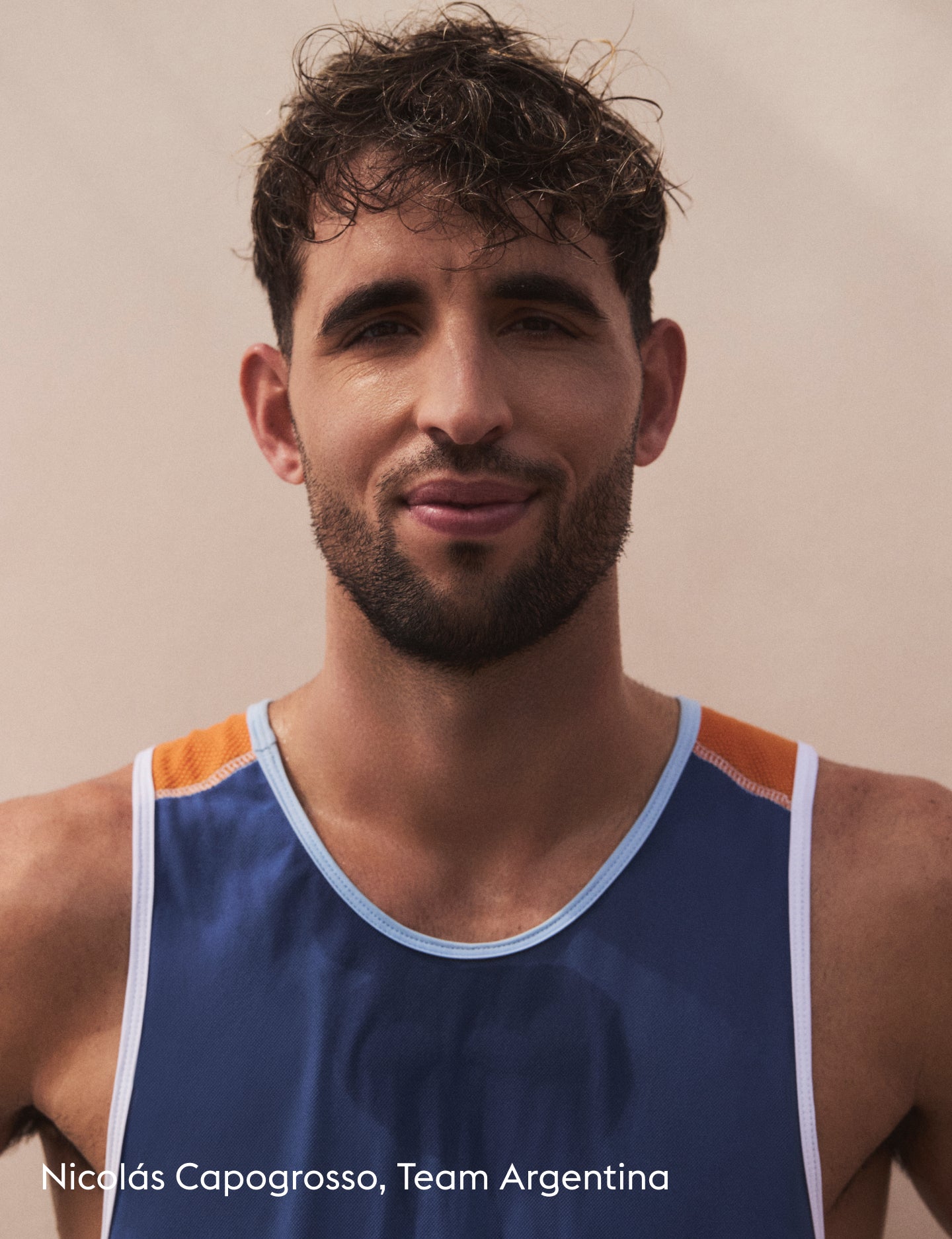 A close-up portrait of a man wearing a blue athletic tank top with orange shoulder panels and white trim, against a plain beige background. White text at the bottom reads 'Nicolás Capogrosso, Team Argentina'.